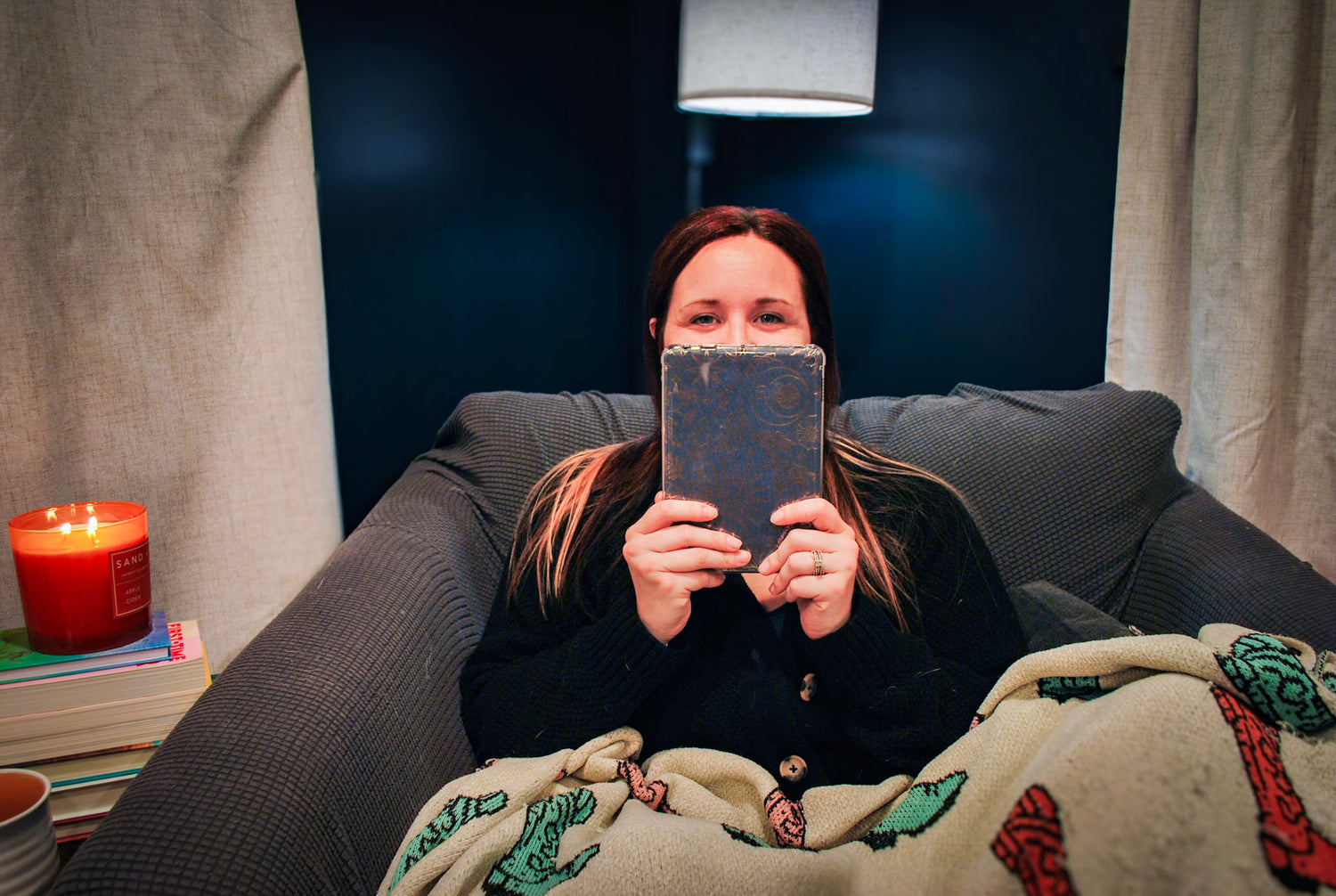 Person reading a book on a couch with a candle and blanket in a cozy setting