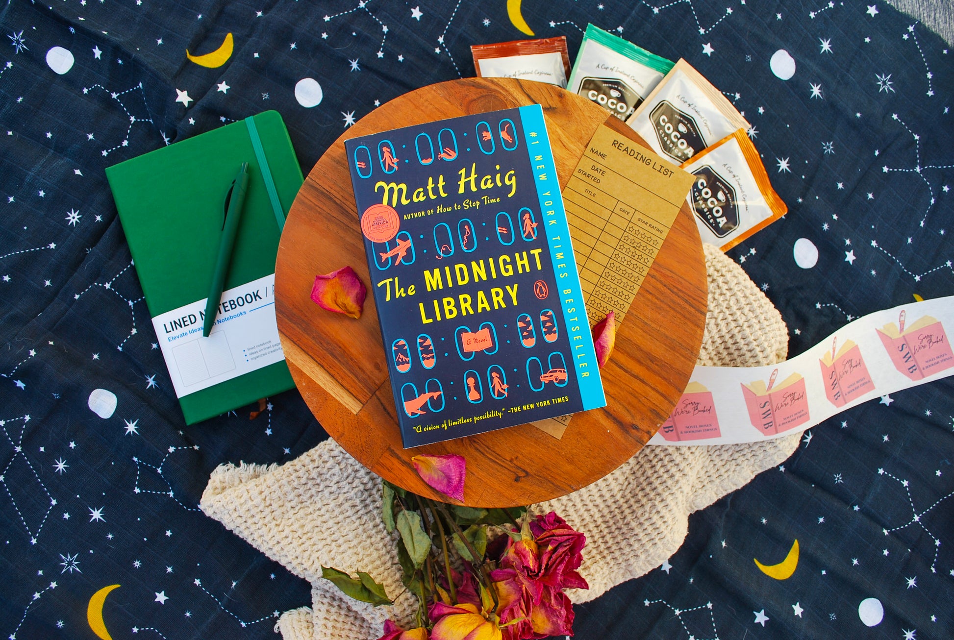 Book titled 'The Midnight Library' by Matt Haig on a wooden table with a starry night background
